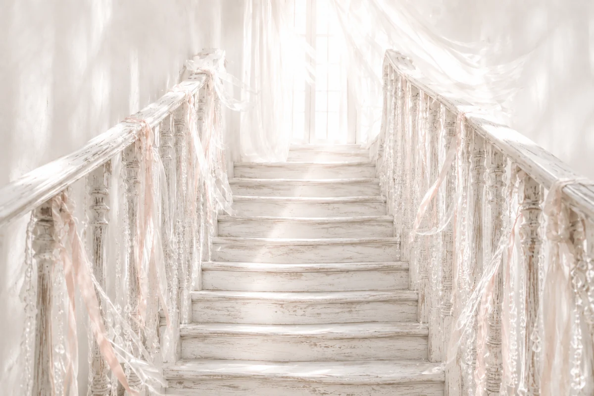 Old whitewashed wooden staircase with blush-pink ribbons and crystal strands leading towards a bright, hazy window.